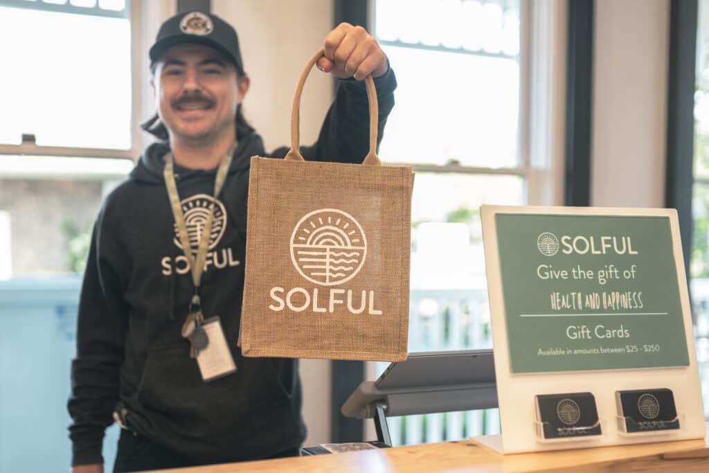 Smiling man holds out a gift bag with the Solful logo on the front